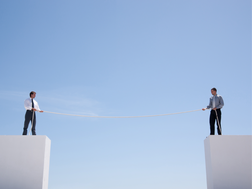 Businessmen standing on wall holding rope.