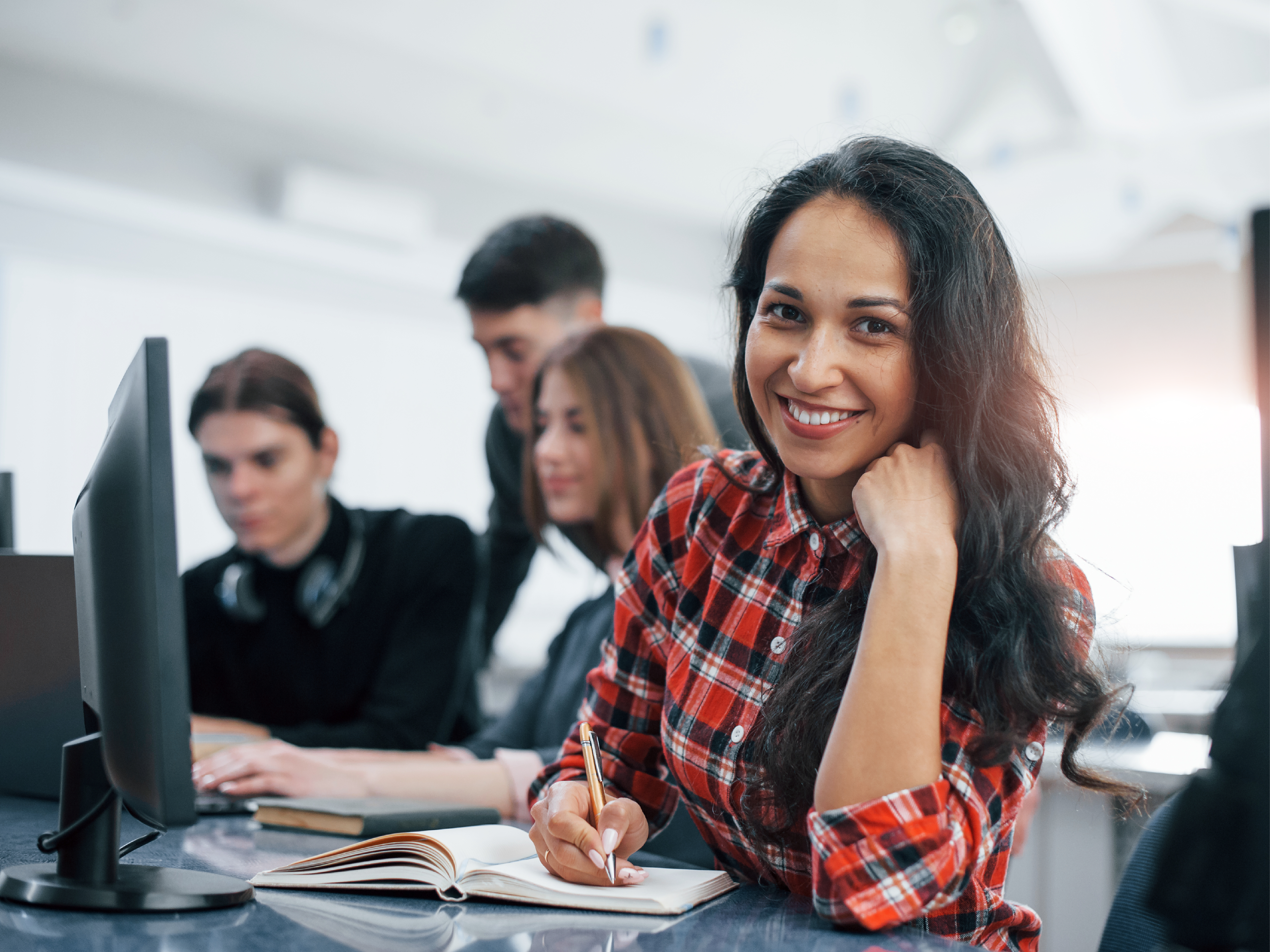 A smiling woman writing notes and her coworkers discussing strategies.