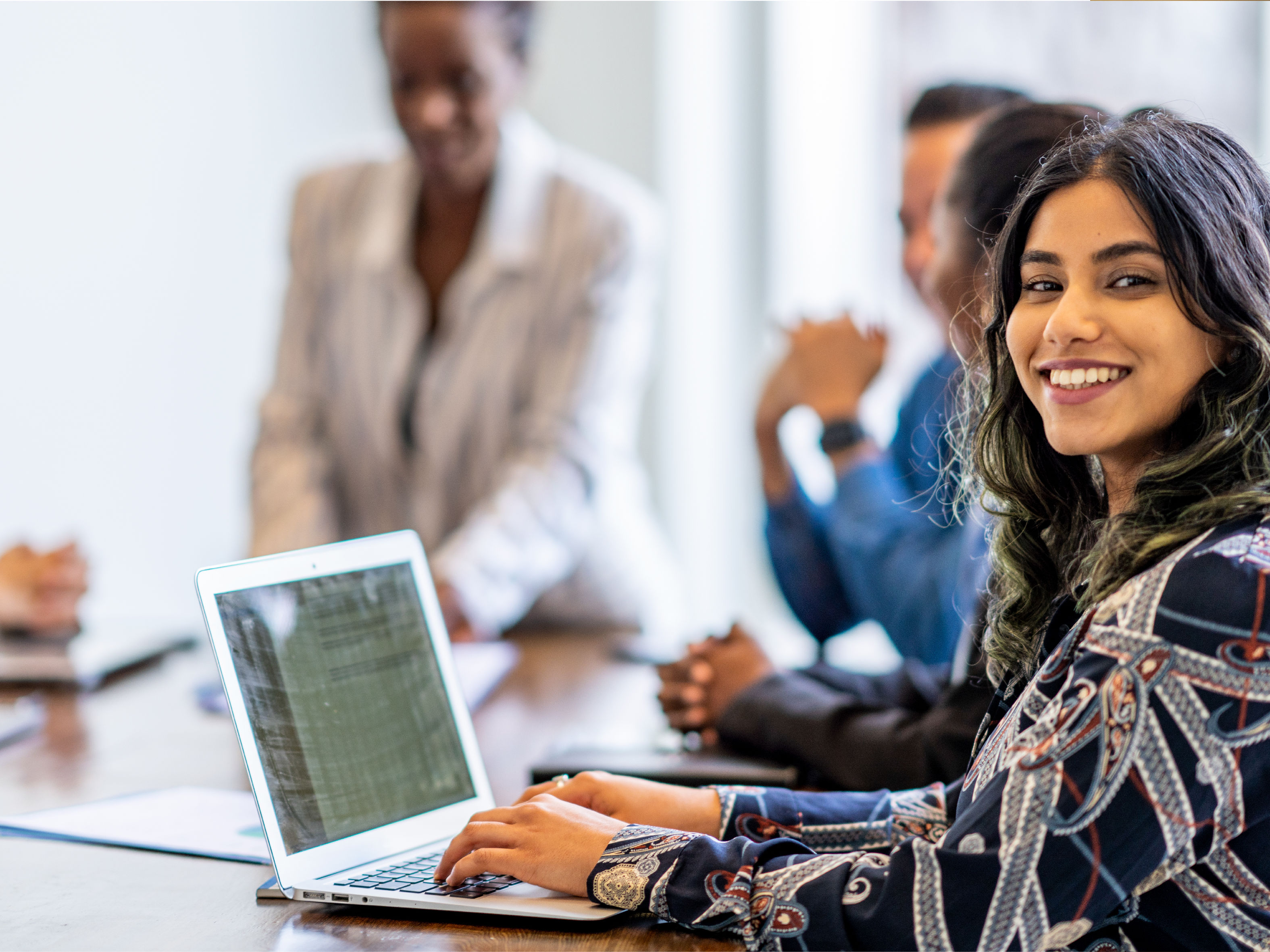 A lady employee with a laptop and teammates, smiling at the camera,